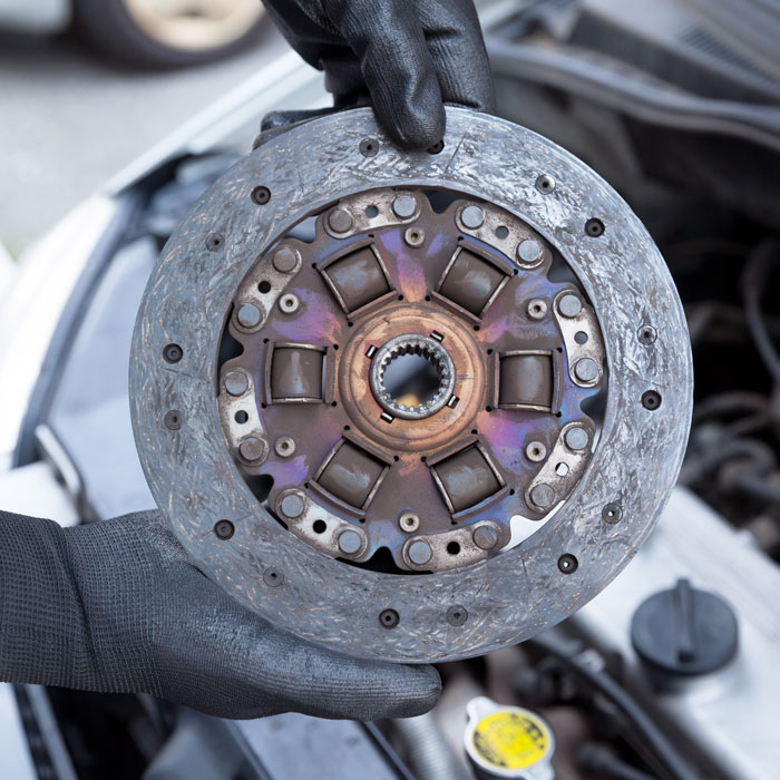 Auto mechanic wearing protective work gloves holds old clutch disc over a car engine